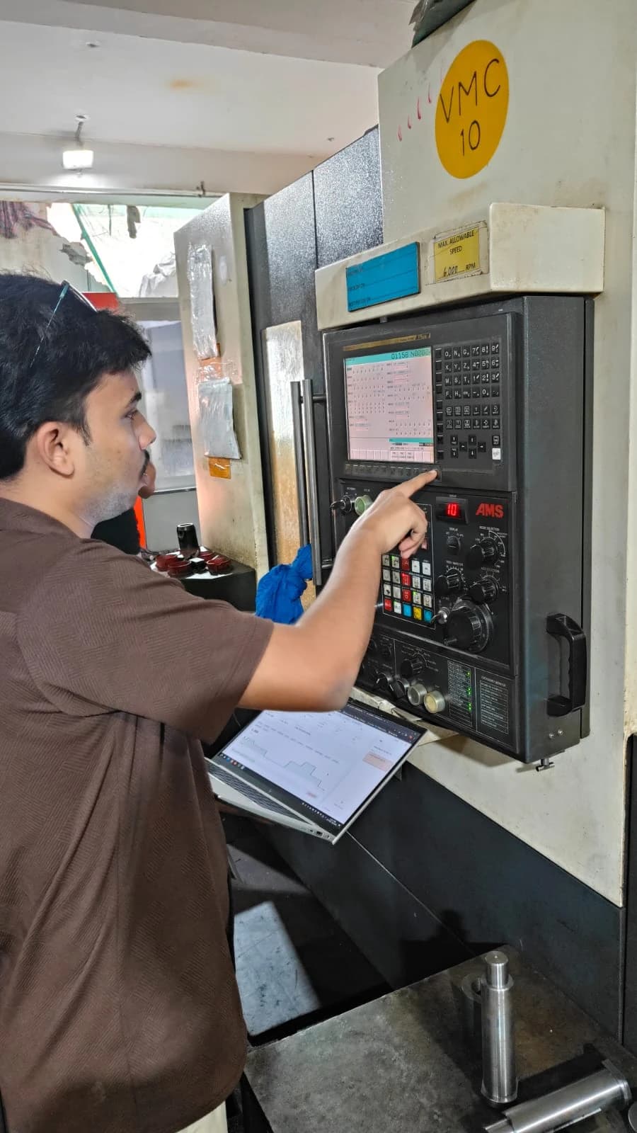 An Algorizz engineer at a CNC machine control panel, holding a laptop showing live LoomOS data